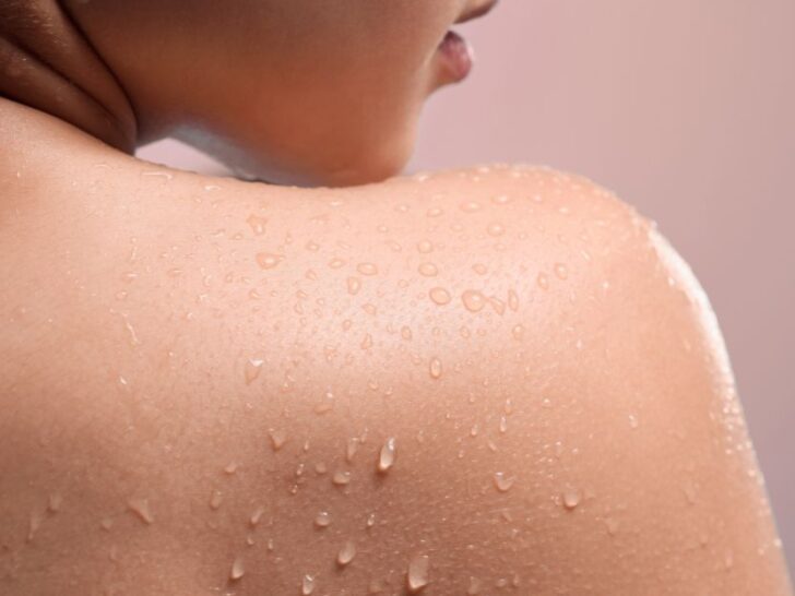 Close-up of a woman's shoulder with water droplets on smooth, glowing skin after a shower, representing full body skincare for women over 40