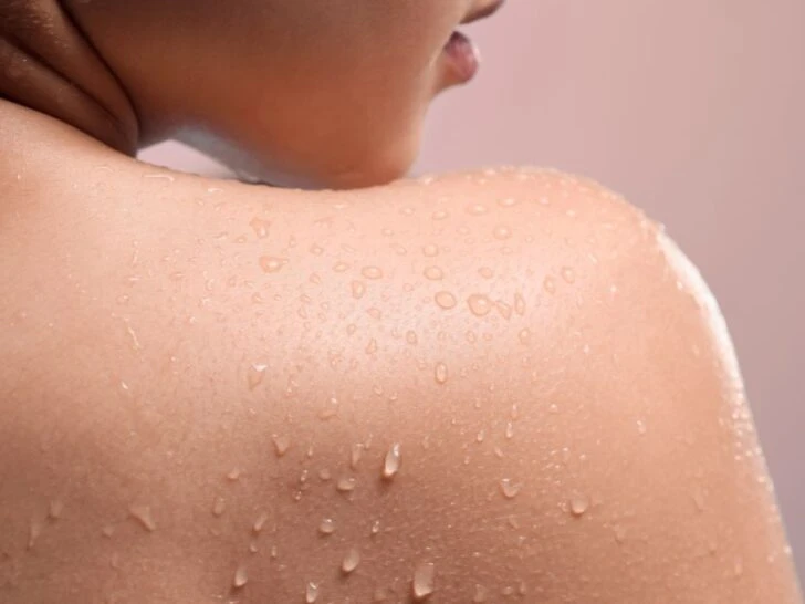 Close-up of a woman's shoulder with water droplets on smooth, glowing skin after a shower, representing full body skincare for women over 40