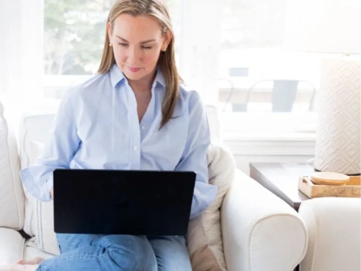 Woman sitting on a sofa shopping online with a laptop, representing smart clothing shopping strategies for 2025