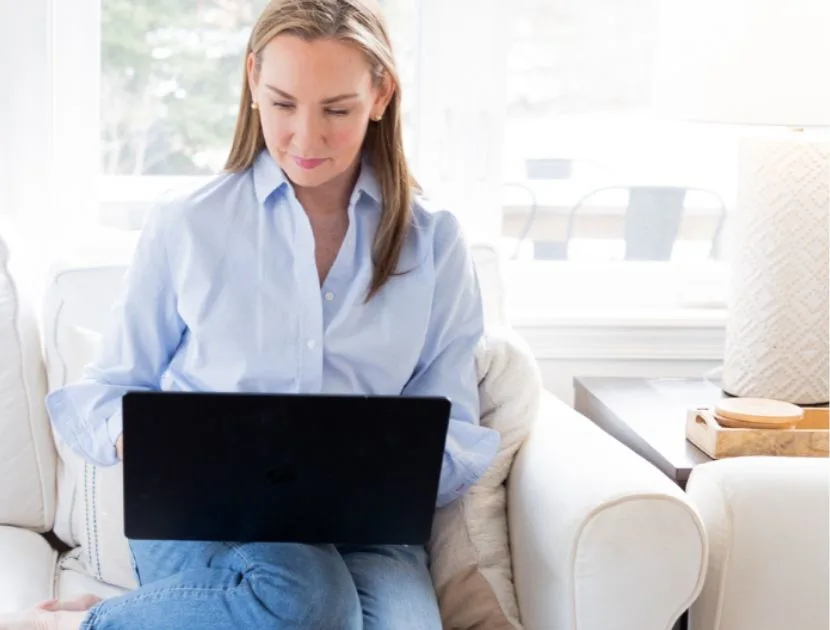 Woman sitting on a sofa shopping online with a laptop, representing smart clothing shopping strategies for 2025