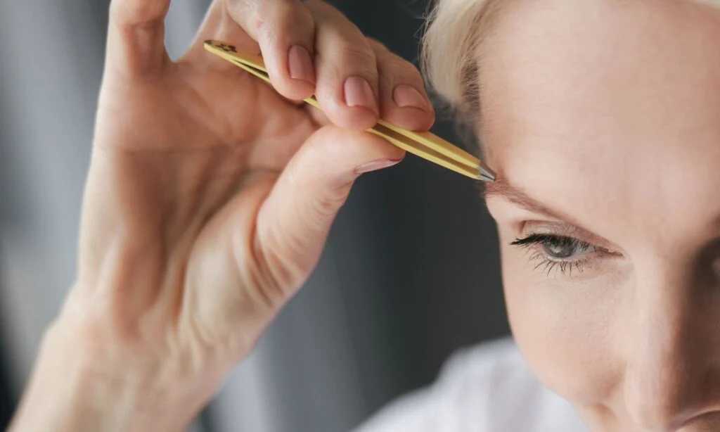 Woman over 40 shaping her eyebrows with tweezers for a natural lift