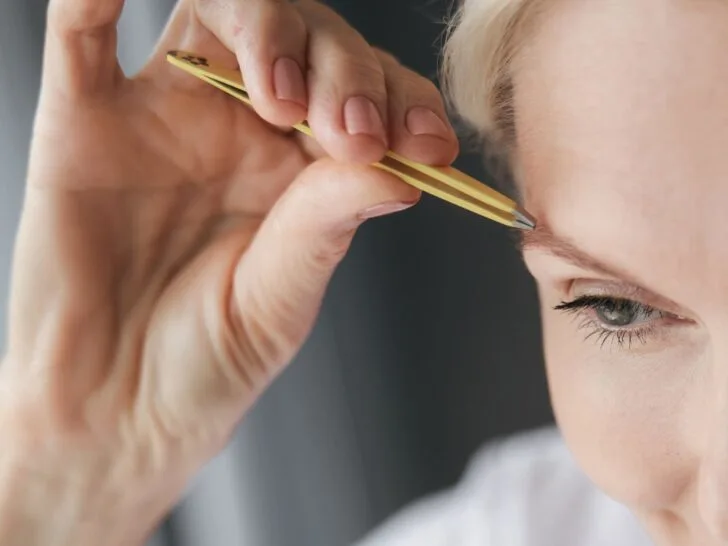 Woman over 40 shaping her eyebrows with tweezers for a natural lift