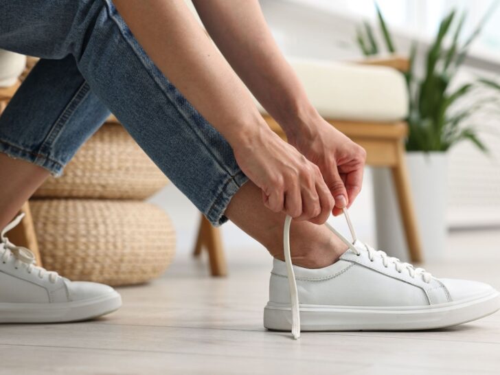 Woman tying classic white sneakers with jeans