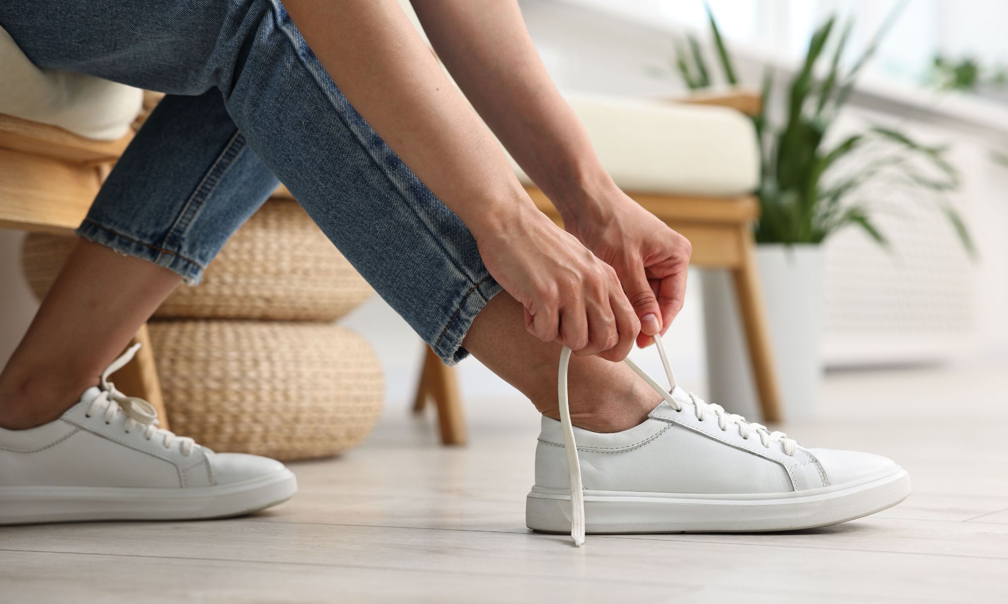 Woman tying classic white sneakers with jeans