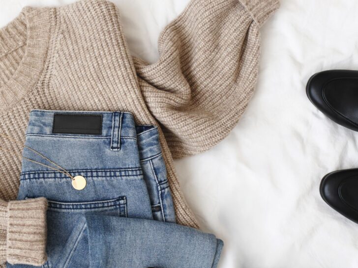 Flat lay of neutral sweater, jeans, and loafers illustrating what to do before buying new clothes to build a cohesive wardrobe.