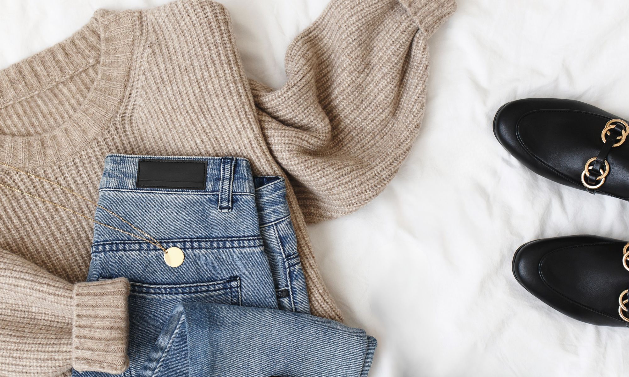 Flat lay of neutral sweater, jeans, and loafers illustrating what to do before buying new clothes to build a cohesive wardrobe.