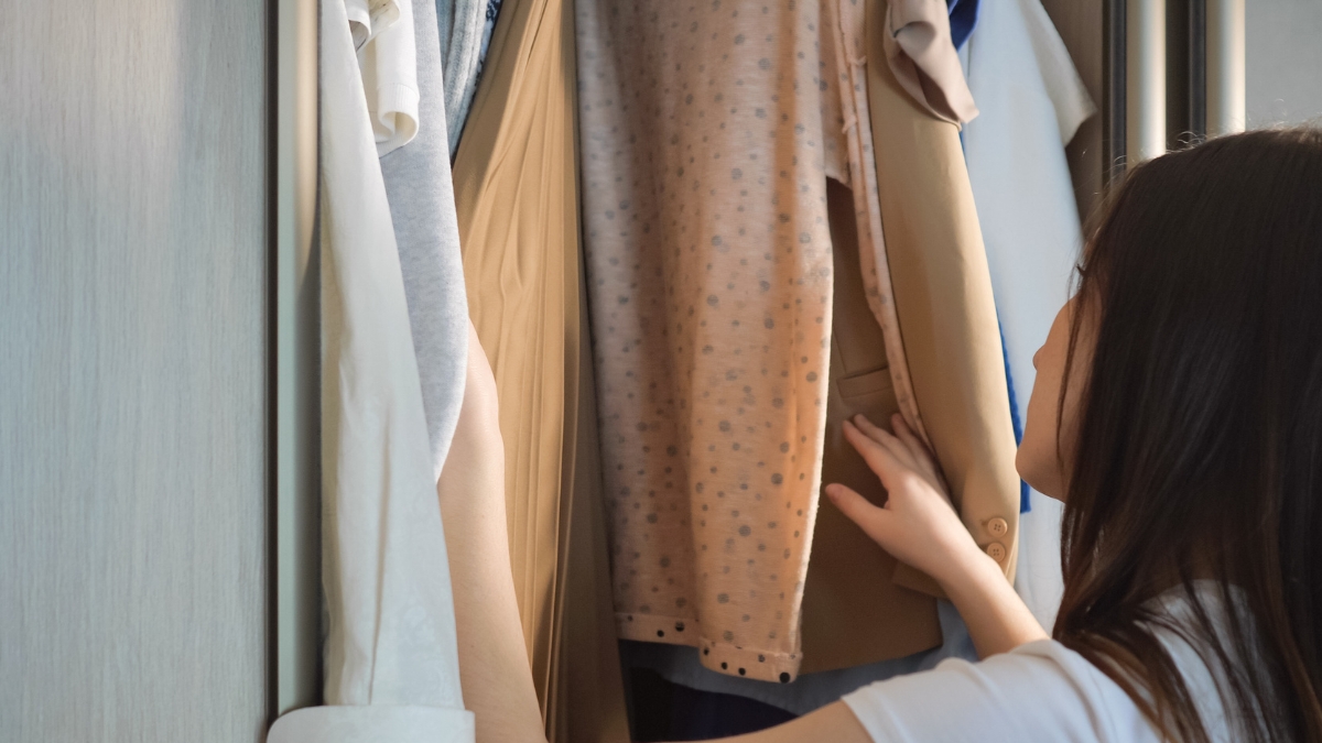 Woman looking through neutral clothes on a closet rail, deciding what to keep during a closet edit
